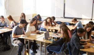 High School Students Sitting At Desks In Classroom Using Laptops