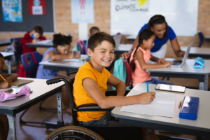 Portrait of disabled boy smiling while sitting on wheelchair in class at elementary school