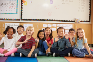 Elementary school kids sitting on classroom floor, smiling for portrait